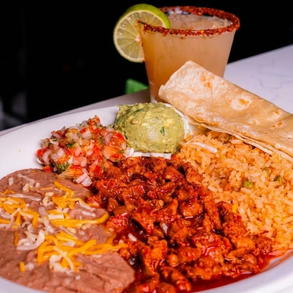 A Mexican platter with rice, beans, meat, guacamole, salsa, tortillas, and a margarita.