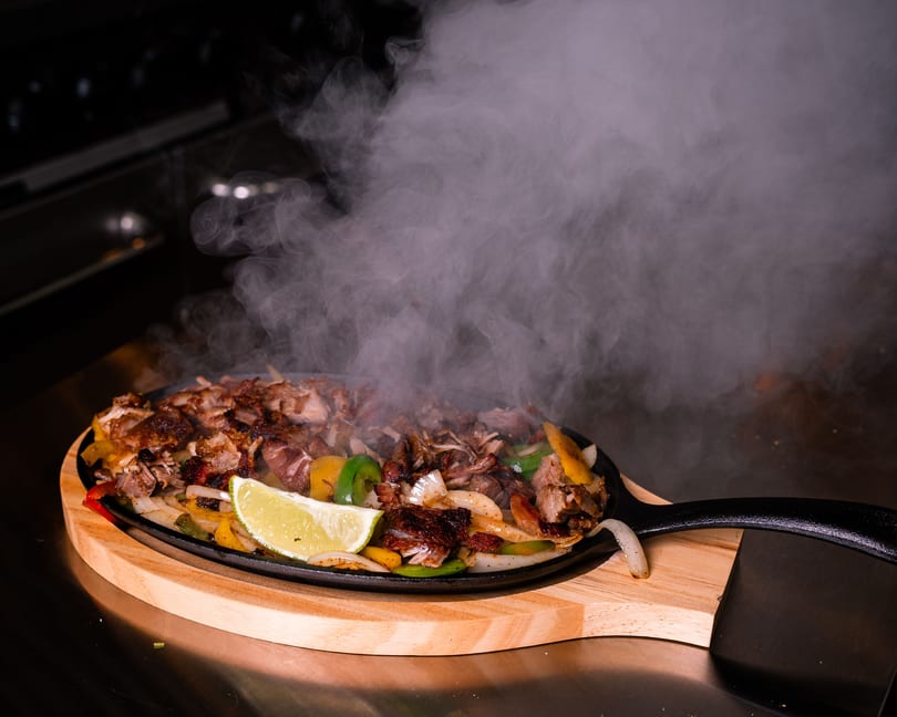 Sizzling fajitas with chicken, peppers, onions, and a lime wedge on a cast iron skillet.